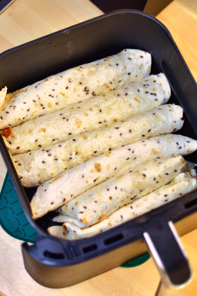 Airfryer Hähnchen Taquitos im korb einer Heißluftfritteuse vorm Backen.