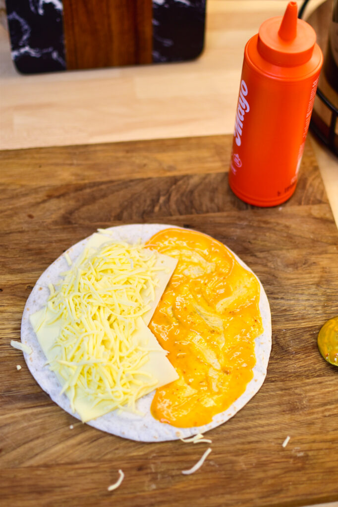 Die Weizentortilla wird zur Hälfte mit Sriracha-Mayo und zur anderen mit Käse belegt.