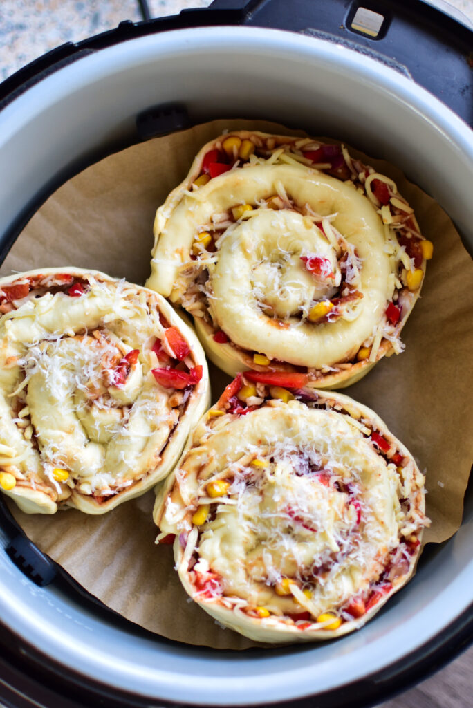 Die Pizzarollen im Korb des Airfryer bevor sie gebacken werden auf einem kleinen Backpapier.