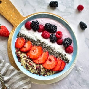Smoothie Bowl mit Erdbeeren, Haferflocken, Chia Samen, Beeren, Schoko Nips und Kokosflocken. Auch Brombeeren und Himbeeren werden darauf verteilt.