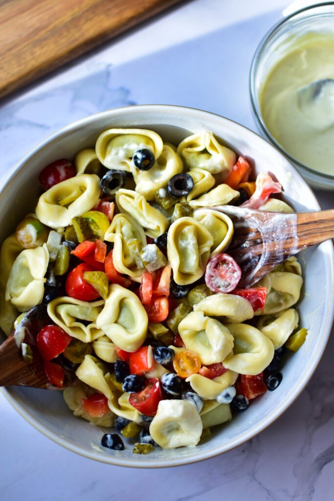 Ein erfrischender Blick von oben auf einen Tortellini Salat mit Joghurt, umgeben von einer Vielzahl von knackigem Gemüse.