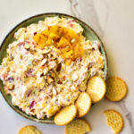 Frischkäse-Ananas-Dip in einer Schale, garniert mit gehackten Mandeln und frischem Koriander.