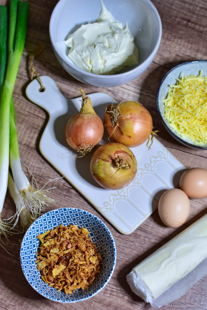 Zutaten für den Zwiebelkuchen im Airfryer: Zwiebeln, Blätterteig, Käse, Schmand, Eier und Frühlingszwiebeln.