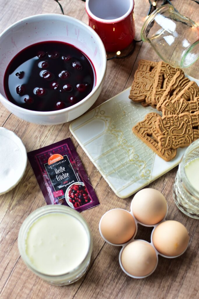 Alle Zutaten für das Weihnachtsdessert auf einen Blick: Kirschen mit Saft, Glühweingewürz, Zucker, Sahne, Gelatine, Spekulatius und Eier. Daneben ein paar kleine Gläser zum Befüllen.