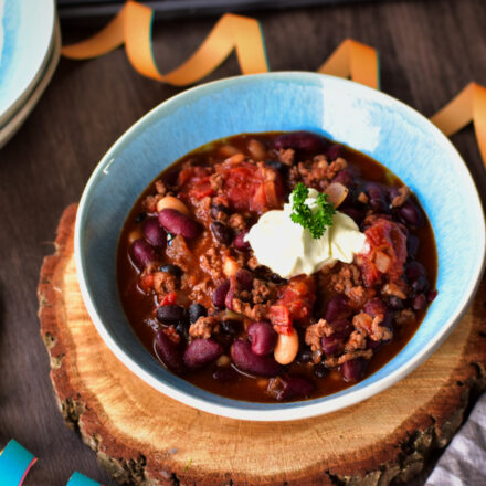Chili con Carne in einer Schüssel, garniert mit Cheddar, Sauerrahm und frischem Koriander – das perfekte Partyrezept mit Hackfleisch und Kaffeenote.