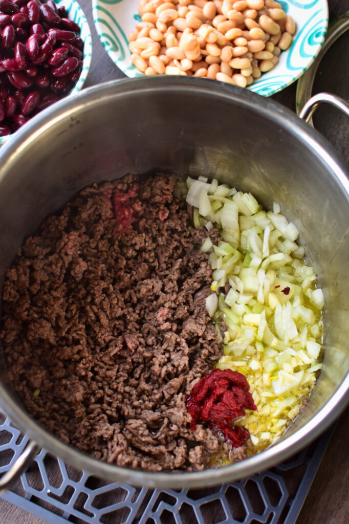 Zubereitung Partychilli. Hackfleisch, Zwiebeln und Tomatenmark in einem großen Topf.