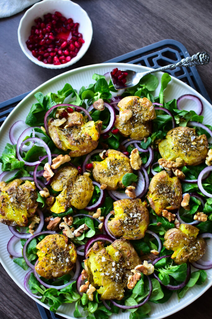 Wintersalat als Smashed Potato Salat mit Walnüssen und Honig-Senf-Dressing auf einem Teller angerichtet