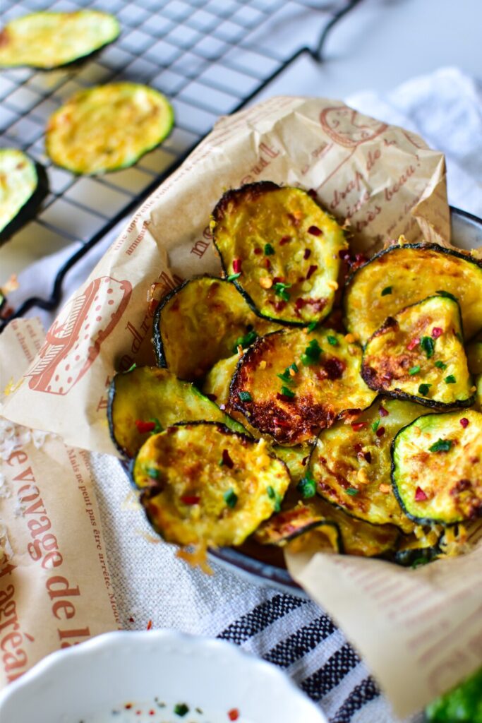 Dünne Zucchinischeiben, gleichmäßig mit Parmesan-Panade bedeckt, knusprig gebacken in der Heißluftfritteuse.