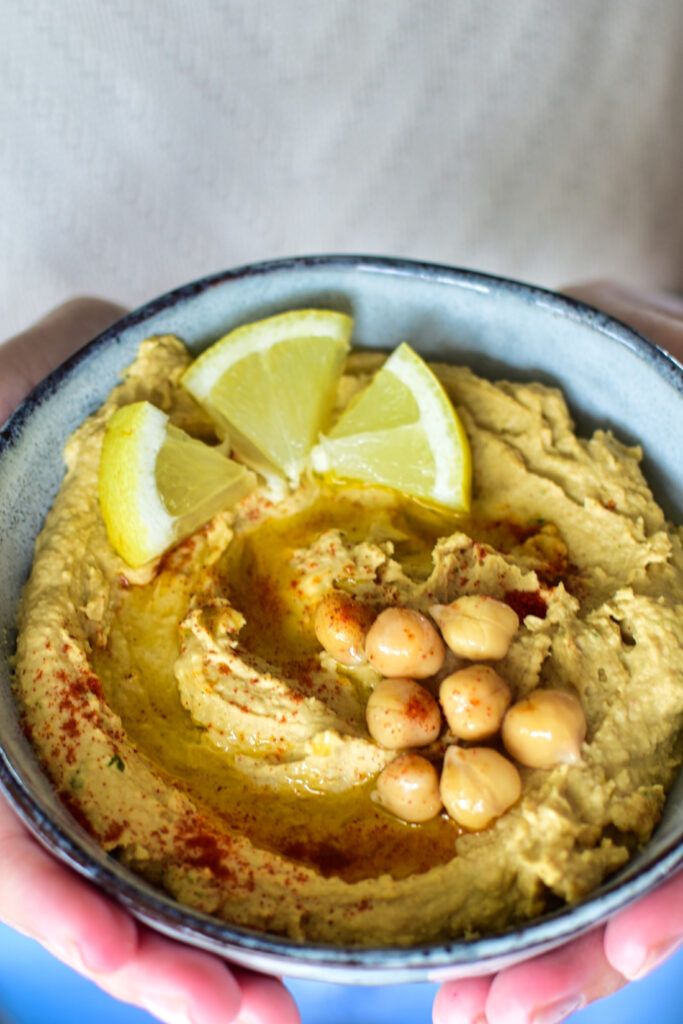 Selbstgemachter Hummus mit Zitronenabrieb, dekoriert mit frischen Zironenstückchen und Paprikapulver.