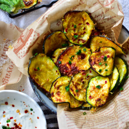 Knusprige Zucchini-Chips mit Parmesan aus der Heißluftfritteuse auf einem Teller mit Backpapier angerichtet.