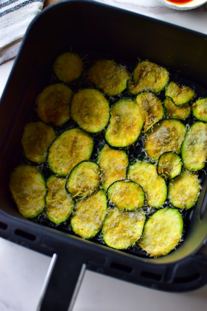 Heißluftfritteuse mit vorbereiteten Zucchini-Chips im Frittierkorb, direkt vor dem Backen.