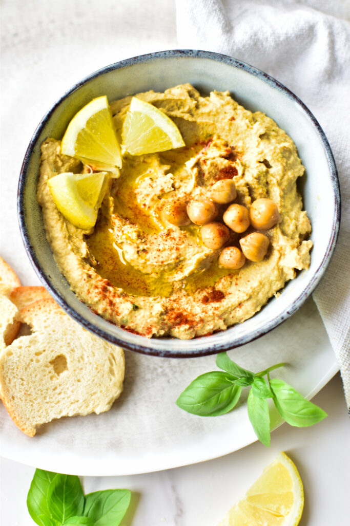 Hausgemachter Hummus mit Zitronennote, serviert mit Basilikum und Gemüsesticks als einfacher Snack.