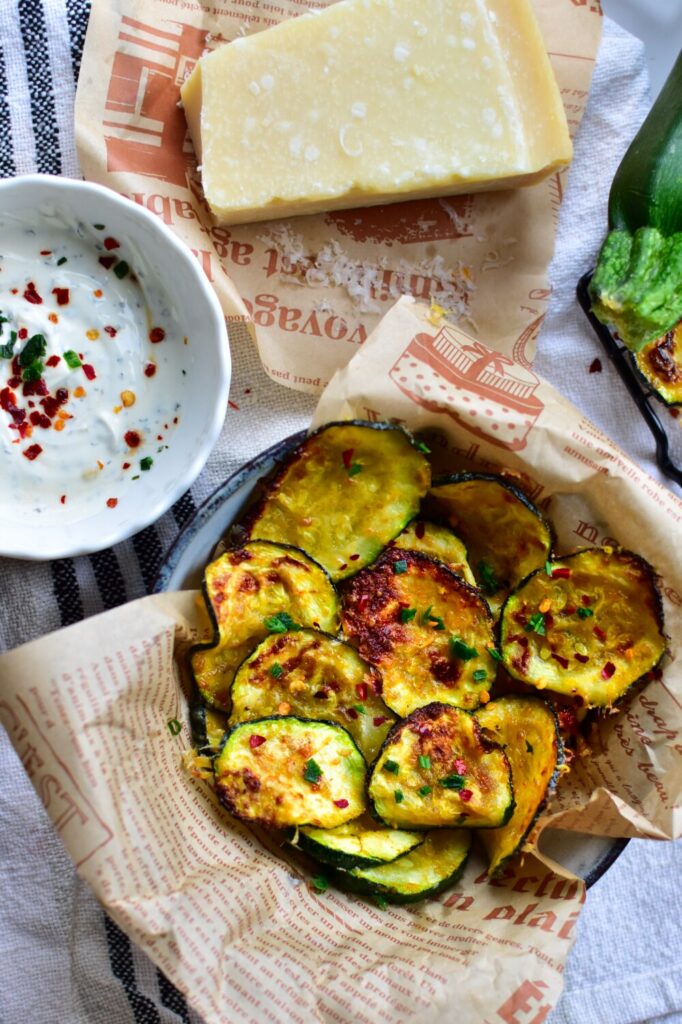 Gesunde und knusprige Zucchini-Chips mit Parmesan, serviert mit einem cremigen Joghurt-Dip.