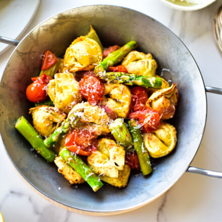 Airfryer Gericht mit Tortellini, Spargel, Tomaten und frischen Kräutern auf einem Teller.