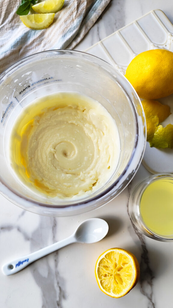 Zitroniges Limoncello Eis im Becher der Ninja Creami Deluxe. Umgeben von Zitronen und Limoncello.
