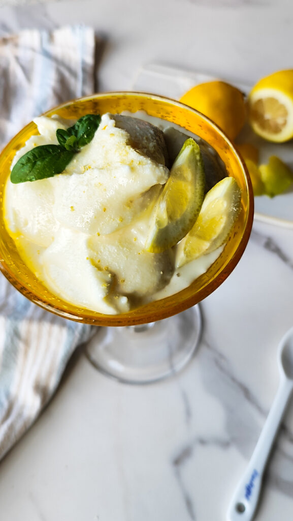 Limoncello Eiscreme selbst gemacht aus der Ninja Creami Deluxe in einem gelben Becher mit einigen Zitronen serviert.