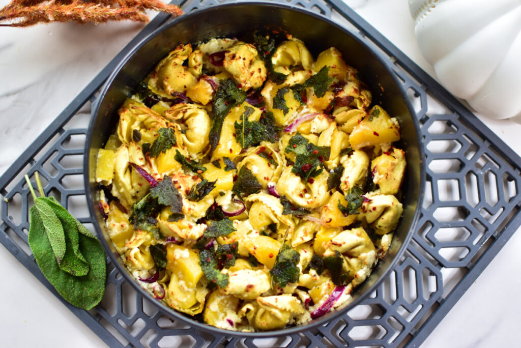 Rezept für herbstlichen Kürbis-Feta-Tortellini-Topf mit frischem Salbei im Topf serviert.