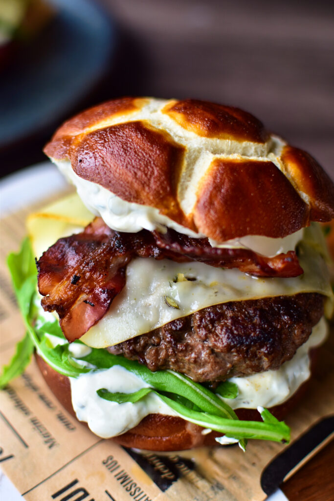 Saftiger Schmand Burger mit Bacon, Käse und Rucola auf Laugenbrötchen – rustikal und cremig zugleich.