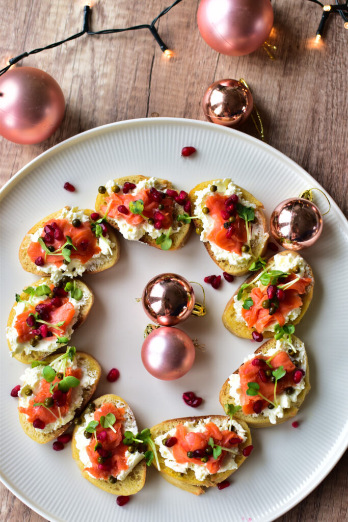 Festliche Vorspeise mit Lachs auf knusprigen Crostini, belegt mit Frischkäse, Kresse und Granatapfel