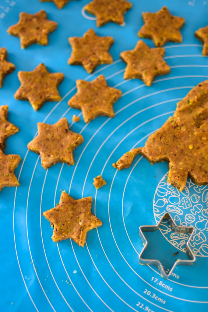 Pistazien Plätzchen werden auf einer Backmatte mit Sternenförmchen ausgestochen.