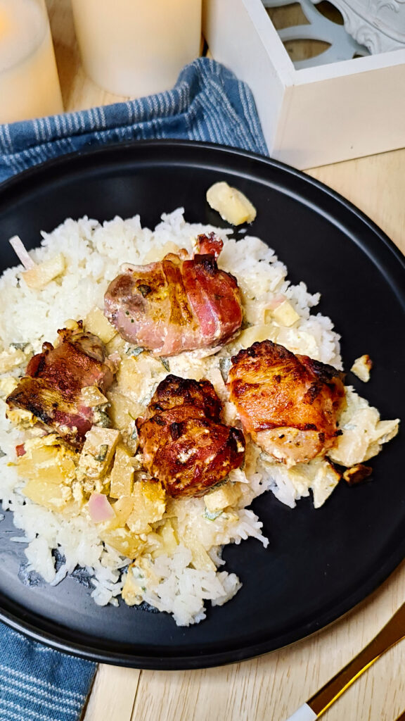 Bacon ummanteltes Schweinefilet goldbraun auf einem schwarzen Teller serviert.