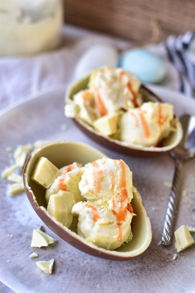 erviertes Ninja CREAMi Deluxe Weiße Schokolade Eis mit gelber Tropen-Sauce in einem Schokoei zu Ostern.