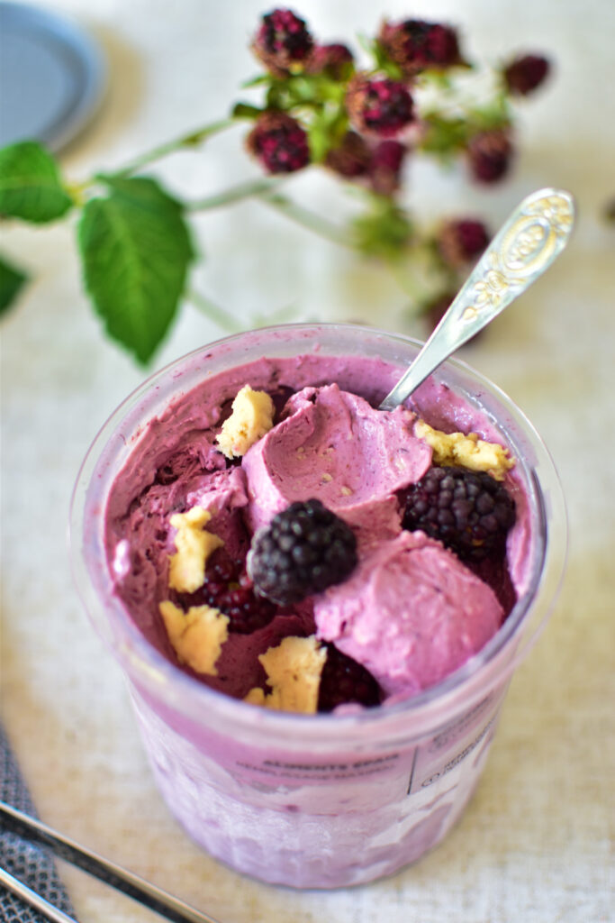 Eine cremige Kugel lila Brombeereis aus der Ninja Creami Deluxe in einer Dessertschale, garniert mit frischen Brombeeren und weichen Keks-Teig-Stückchen.