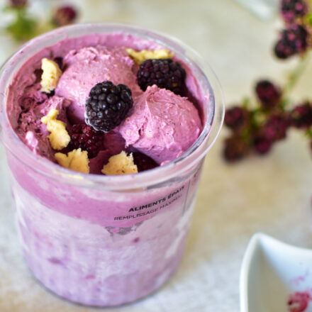 Ein Ninja Creami Becher gefüllt mit lilafarbenem Brombeereis mit Keksteig-Stückchen.
