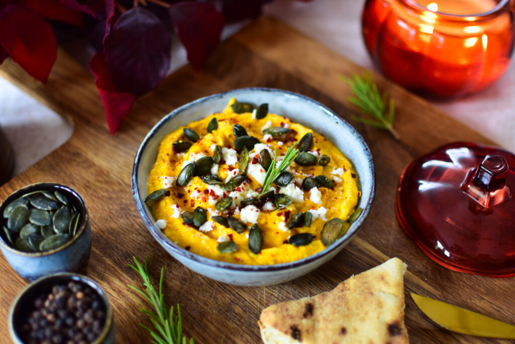 Cremiger Kürbis Dip mit Feta serviert mit einer Scheibe frisch gebackenem Fladenbrot und Kürbiskernen.