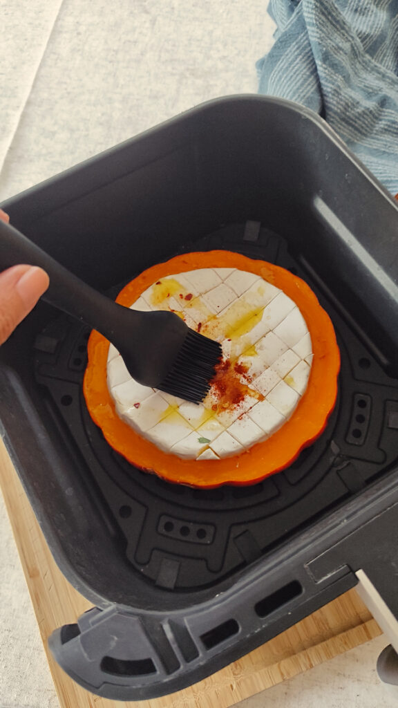 Halbierter Hokkaido-Kürbis nach dem Vorgaren in der Heißluftfritteuse wird eingepinselt.
