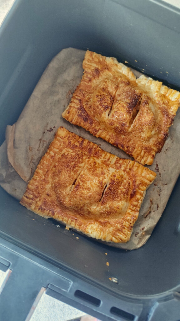 Frisch gebackene knusprige Apfeltaschen im Korb der Heißluftfritteuse mit Zimtzucker-Kruste.