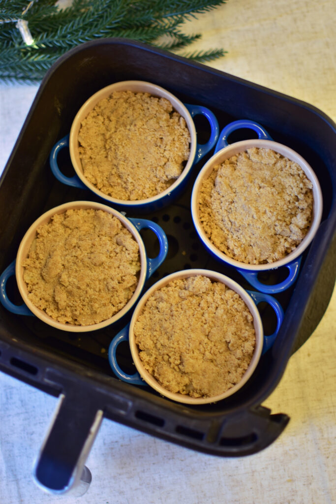 Vier kleine Keramikförmchen mit Birnencrumble, vorm Backen in der Heißluftfritteuse: Ideales Weihnachtsdessert zum Vorbereiten.