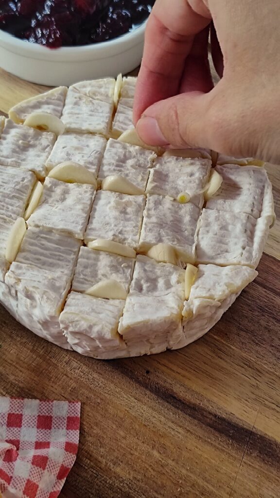 Der Ofenkäse wird mit dünnen Scheiben Knoblauch gefüllt.