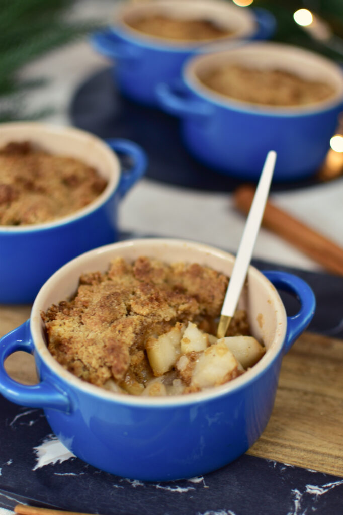 Birnencrumble aus dem Airfryer in blauen Mini-Auflaufformen, vorne eine Portion mit Löffel und saftigen Birnenstücken.