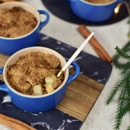 Vier kleine Birnencrumbles mit goldbrauner Streuseldecke in blauen Keramikförmchen.
