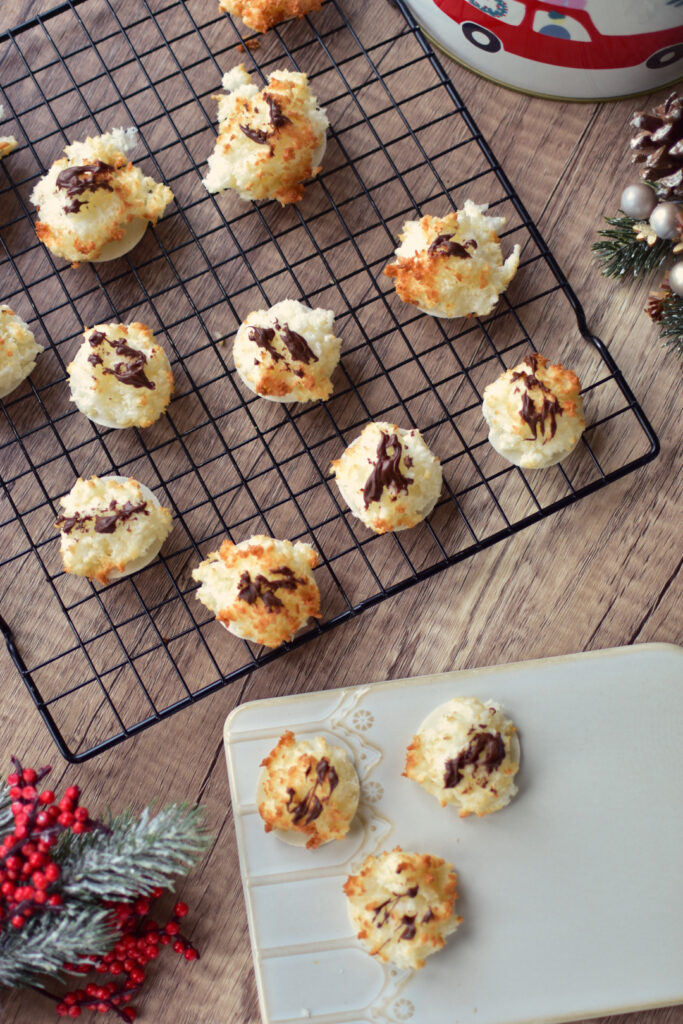 Fertige Kokosmakronen mit geschmolzener Zartbitterschokolade auf einer weihnachtlich dekorierten Platte