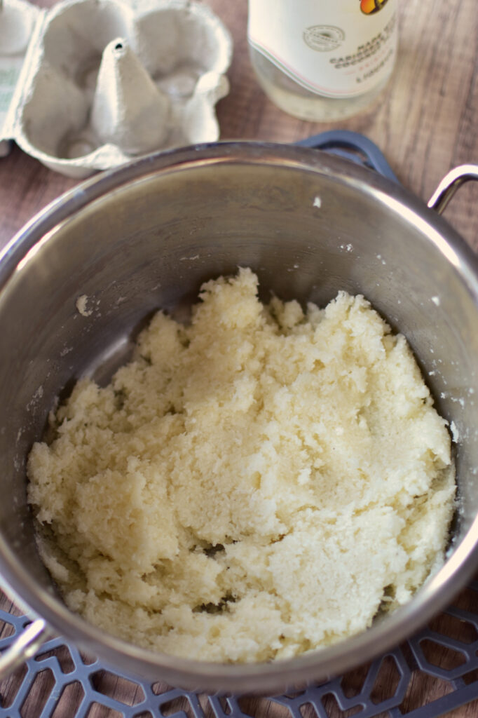 Erwärmte Kokosmasse aus Kokosraspeln, Eiweiß und Zucker in einem Edelstahltopf