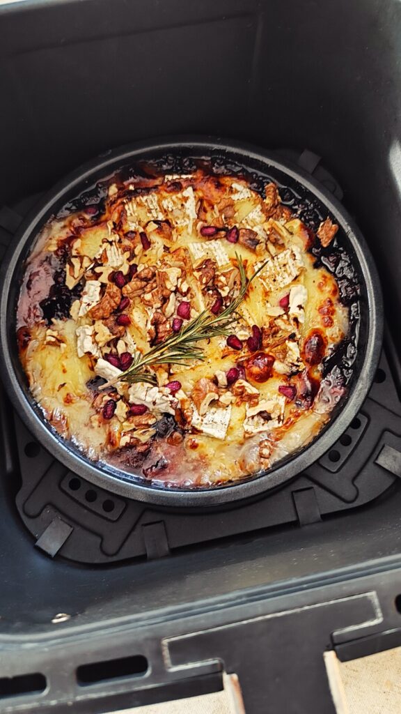 Geschmolzener Ofenkäse im Korb des Ninja Airfryer mit Wildpreiselbeeren in einer kleinen Auflaufform.